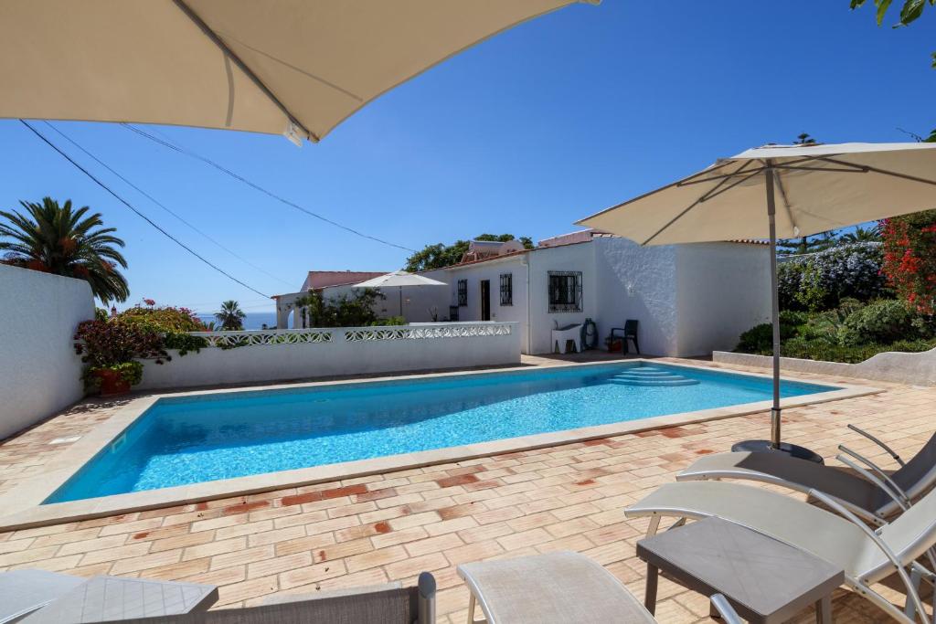 a swimming pool with chairs and an umbrella at Villa Mirembe in Luz