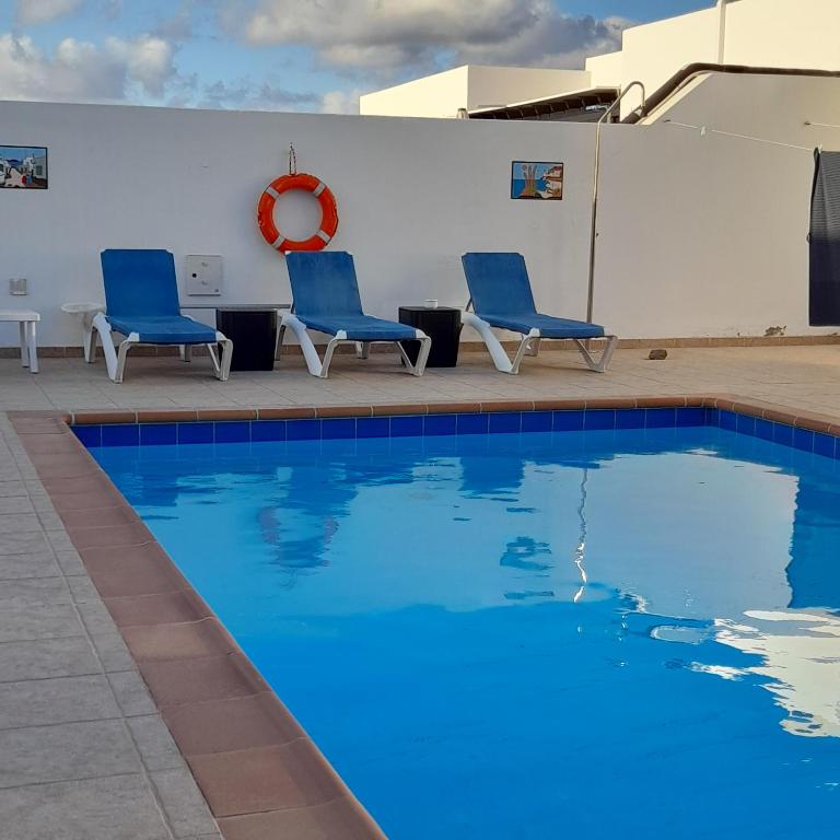 uma piscina com duas cadeiras azuis ao lado de um edifício em Villa julima em Playa Blanca