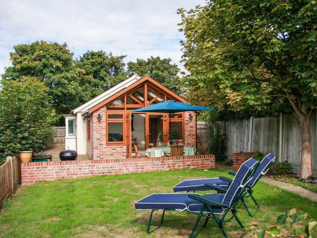 a small cabin with chairs and an umbrella in a yard at The Seaside Cottage in Gorleston-on-Sea