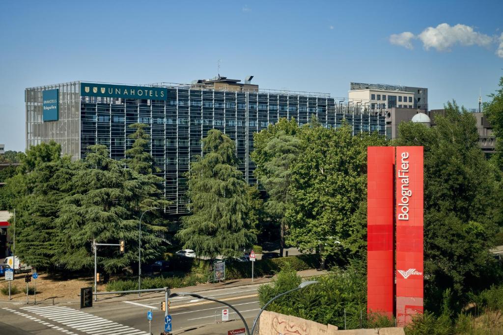 un grande edificio con un cartello rosso davanti agli alberi di UNAHOTELS Bologna Fiera a Bologna