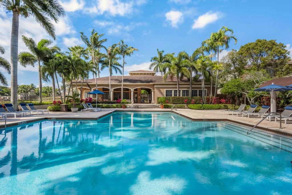 a swimming pool in front of a house with palm trees at Luxurious Apartments with Pool and Gym at Boynton Beach in Boynton Beach