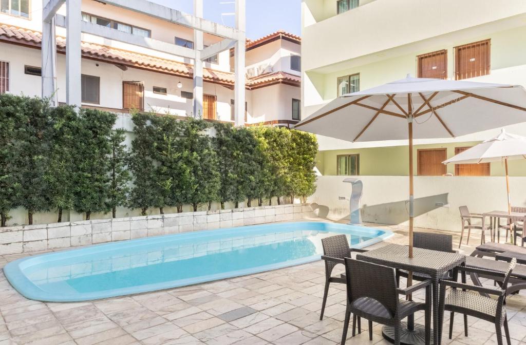 una piscina con tavoli, sedie e ombrellone di Praia Residence a Porto De Galinhas