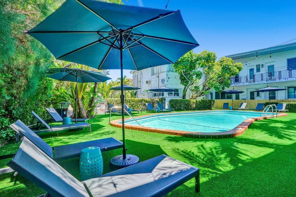 uma piscina com um guarda-sol azul e algumas cadeiras e uma mesa em Bay Harbor Suites em Miami Beach