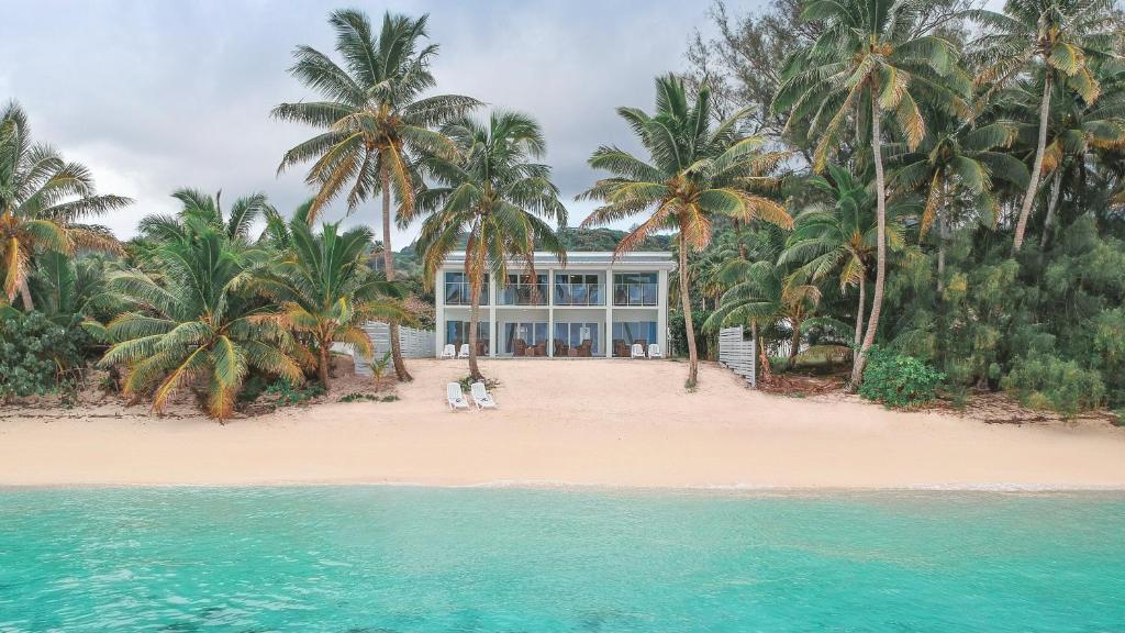 une maison sur une plage avec des palmiers et l'eau dans l'établissement Vaima Beachfront Apartments, à Rarotonga