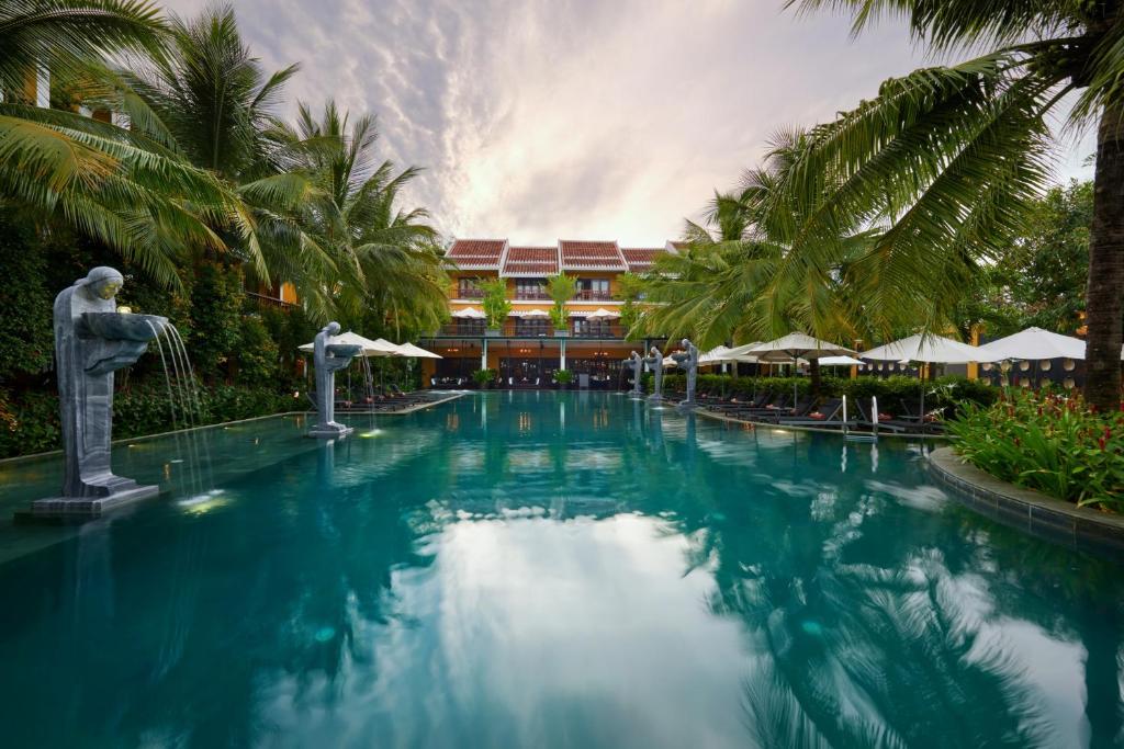 una piscina frente a un complejo con palmeras en La Siesta Hoi An Resort & Spa en Hoi An