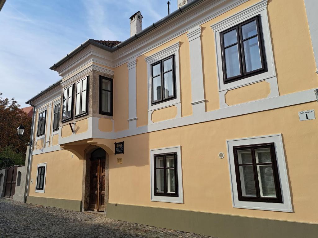 a yellow house with black windows on a street at Bem Villa Apartman, Kőszeg in Kőszeg