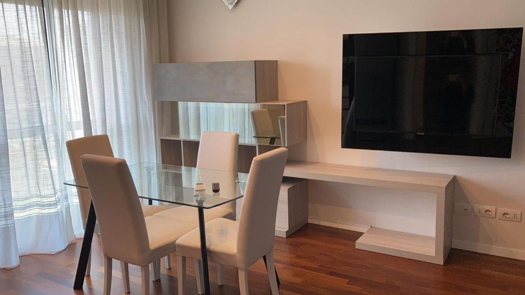 una sala da pranzo con tavolo in vetro, sedie e TV di Achille Apartment a Milano