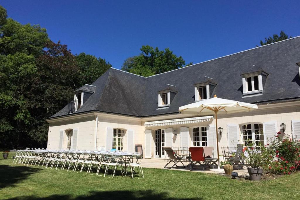 a white house with tables and chairs in the yard at Spacious house in a wooded park enclosed by walls and its swimming pool in Saint-Cyr-sur-Loire