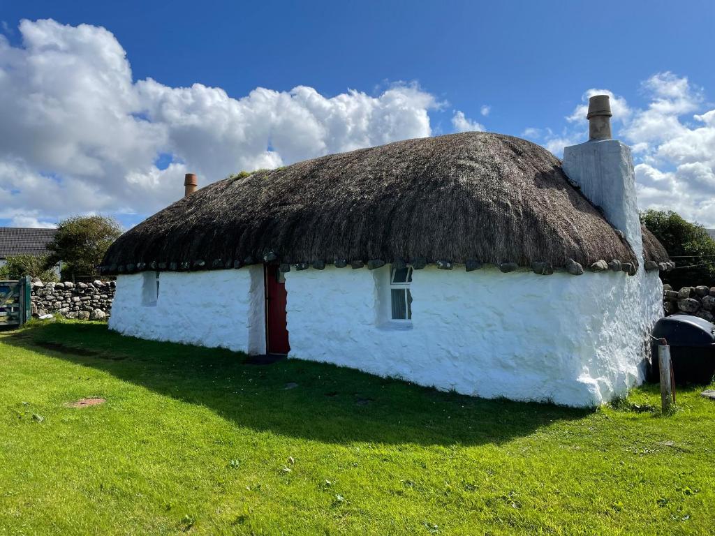 ein altes weißes Cottage mit einem Strohdach in der Unterkunft Beaton's Croft House - Uig Skye in Portree