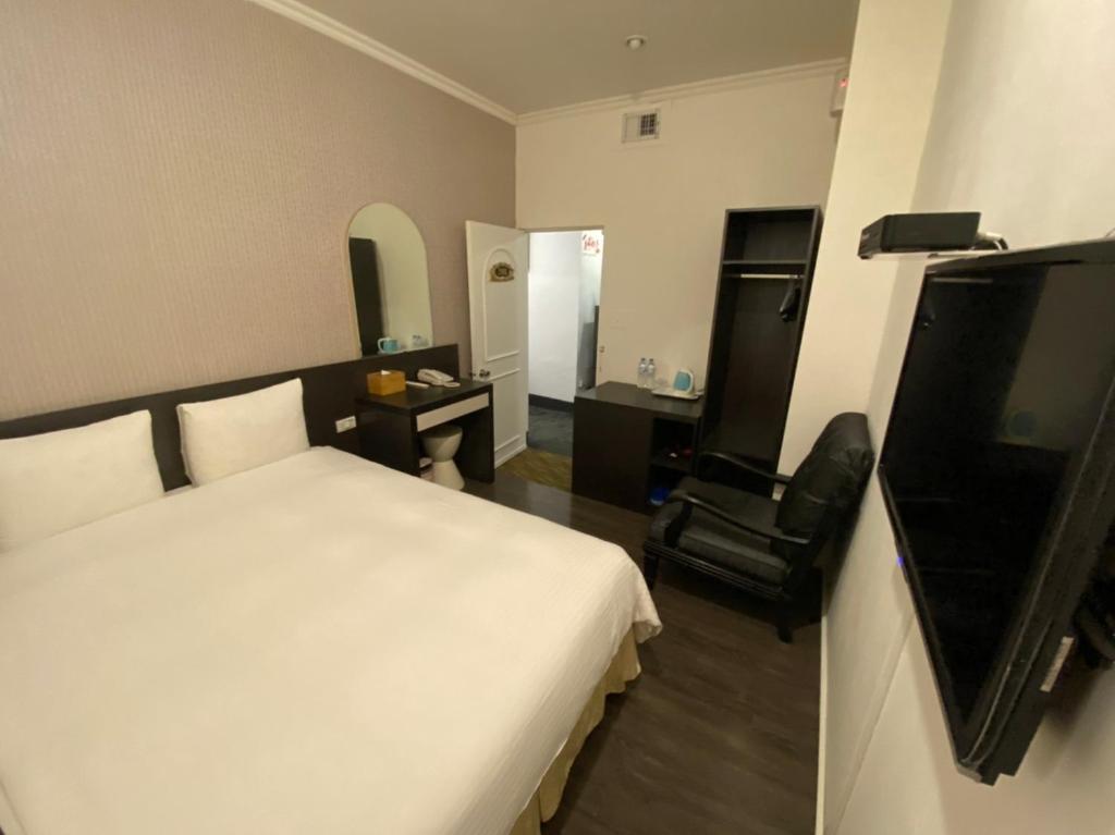 Queens Hotel في تايبيه: غرفة نوم بسرير ابيض ومكتب وكرسي