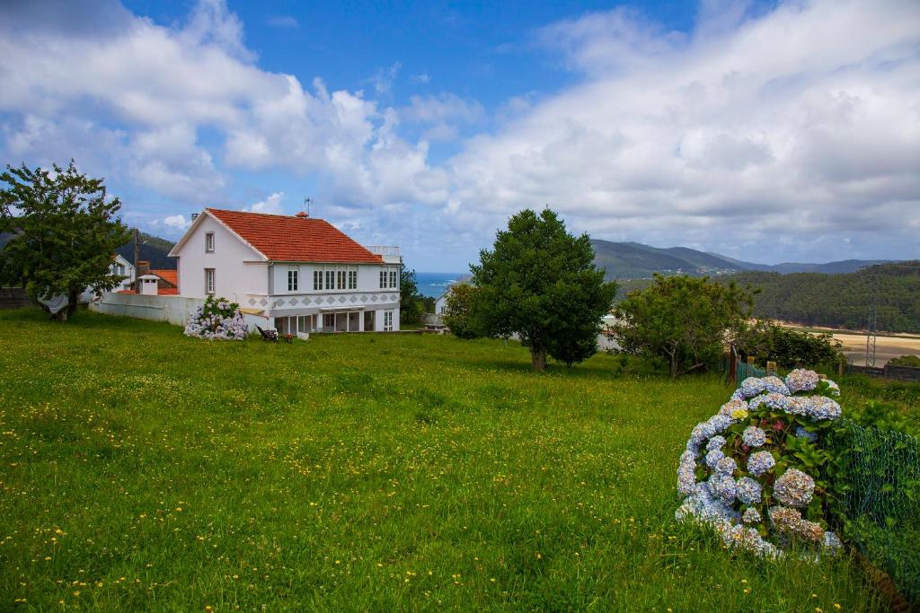 una casa en una colina con un campo verde con flores en Beachfront Surf & Remote Work House, en Valdoviño