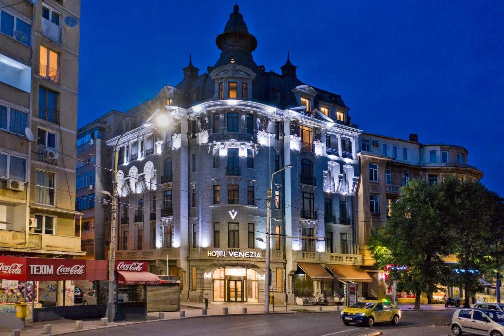 a lit up building on a city street at night at Hotel Venezia by Zeus International in Bucharest
