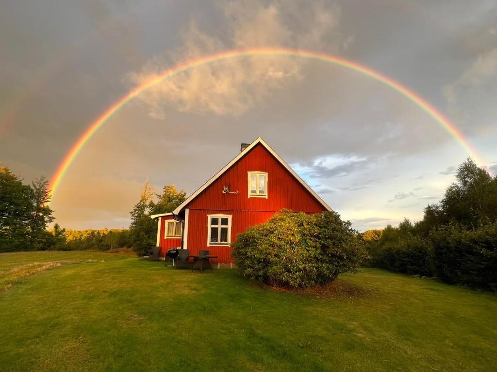 un arco iris sobre una casa roja en un campo en Slättsjö, en Slättsjö