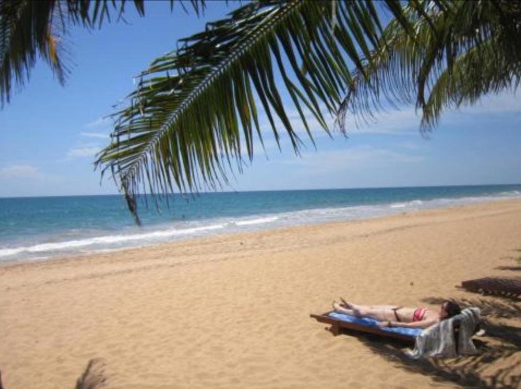 a person laying on a beach under a palm tree at Janus Paradise Rest in Bentota