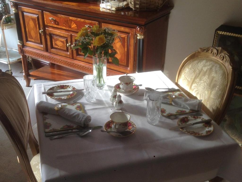 a table with a white table cloth and a vase of flowers at Melody House in Fakenham