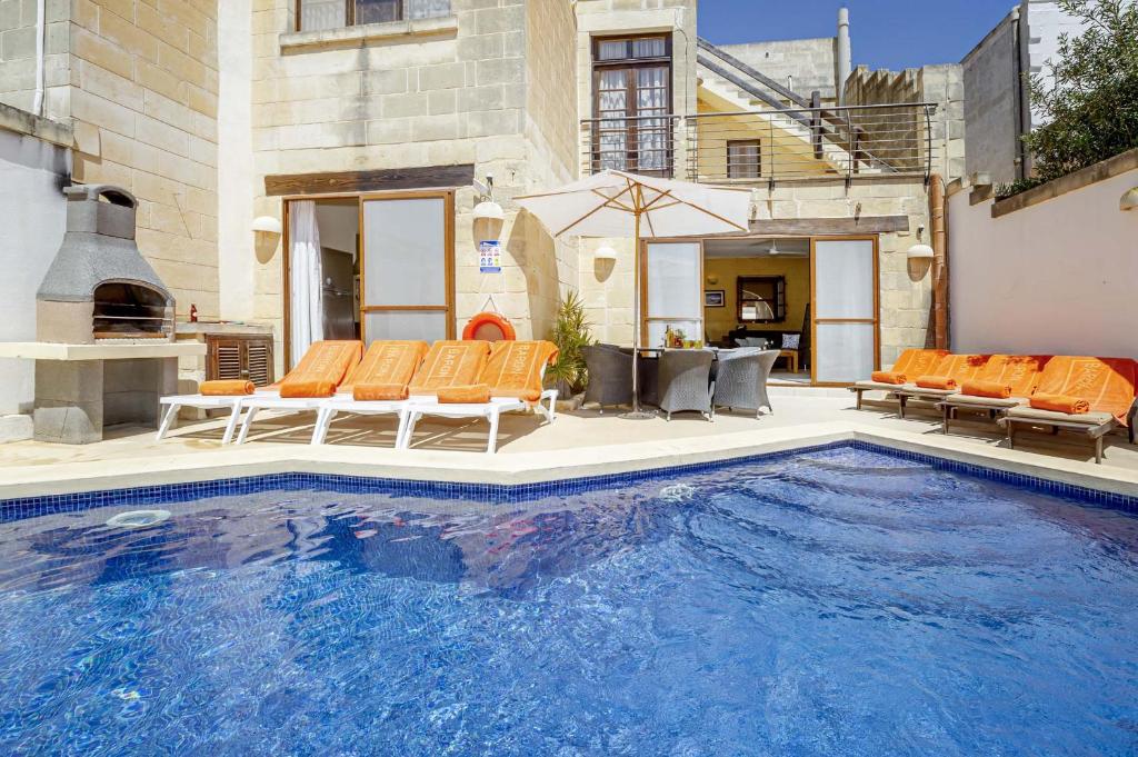 a large swimming pool with orange chairs next to a house at Razzett Luna Holiday Home in Xagħra
