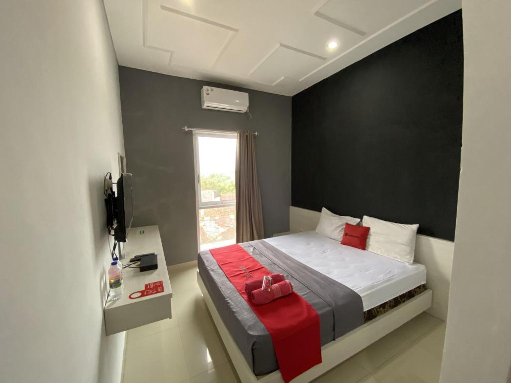a bedroom with a bed with red sheets and a window at RedDoorz near RSUD Margono Purwokerto 3 in Purwokerto