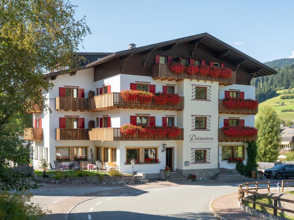 a large white building with red flowers on balconies at Hotel Dolomiten in Monguelfo