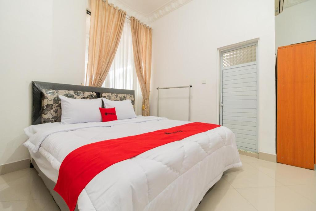 um quarto com uma grande cama branca e um cobertor vermelho em RedDoorz Syariah near Universitas Putra Indonesia Padang em Kampungdurian