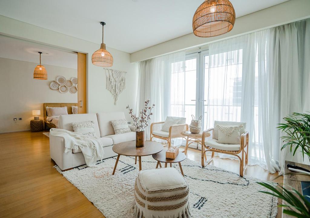 a living room with white furniture and a large window at Nasma Luxury Stays - Serene Apartment With Balcony Steps From The Sea in Abu Dhabi