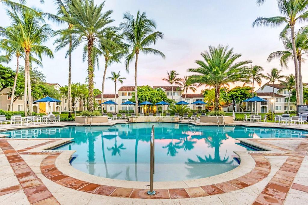 a swimming pool with palm trees and blue umbrellas at Stunning & Spacious Apartments at Miramar Lakes in South Florida in Miramar