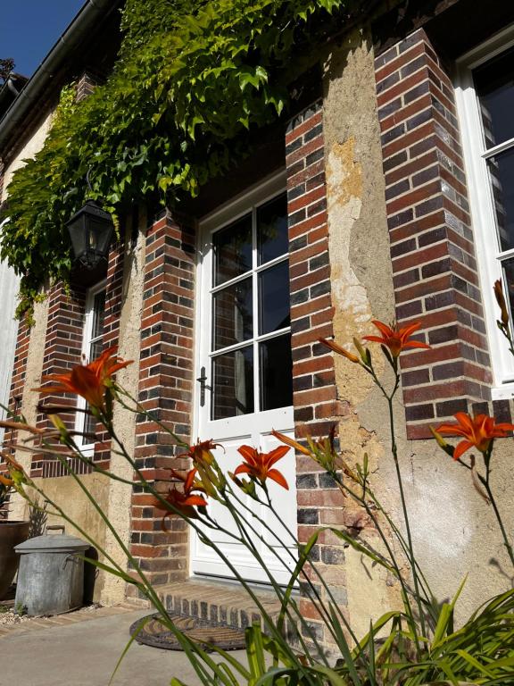ein Backsteinhaus mit einer weißen Tür und Blumen in der Unterkunft La maison du Gardien - LE PRIEURÉ DU PREUX 