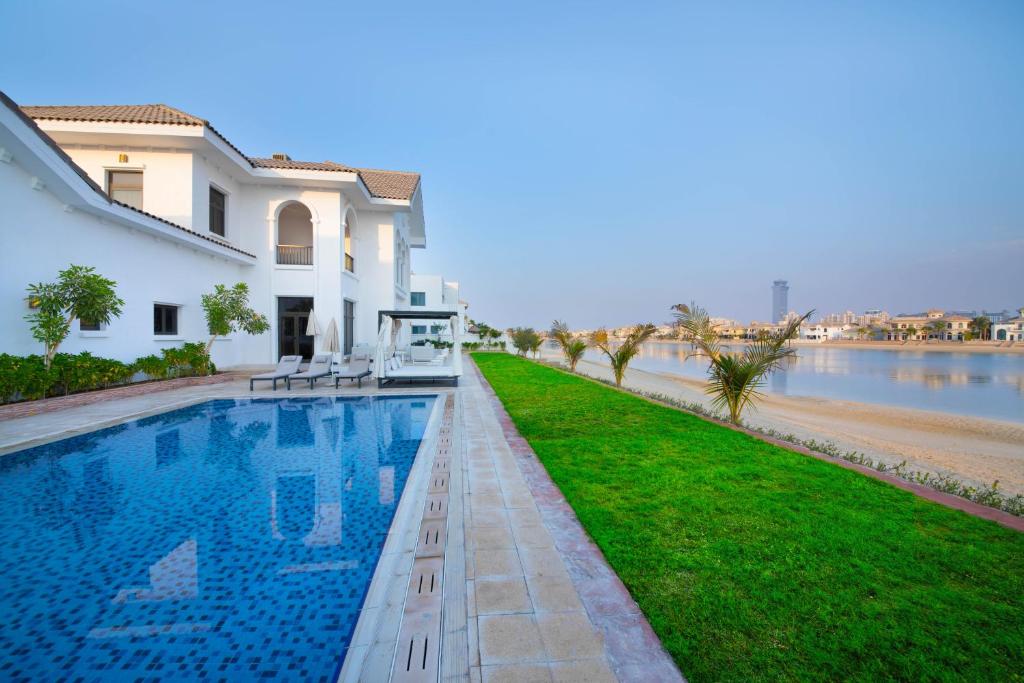 a villa with a swimming pool next to a body of water at Maison Privee - Luxury Villa with Dramatic View Private Beach & Pool in Dubai