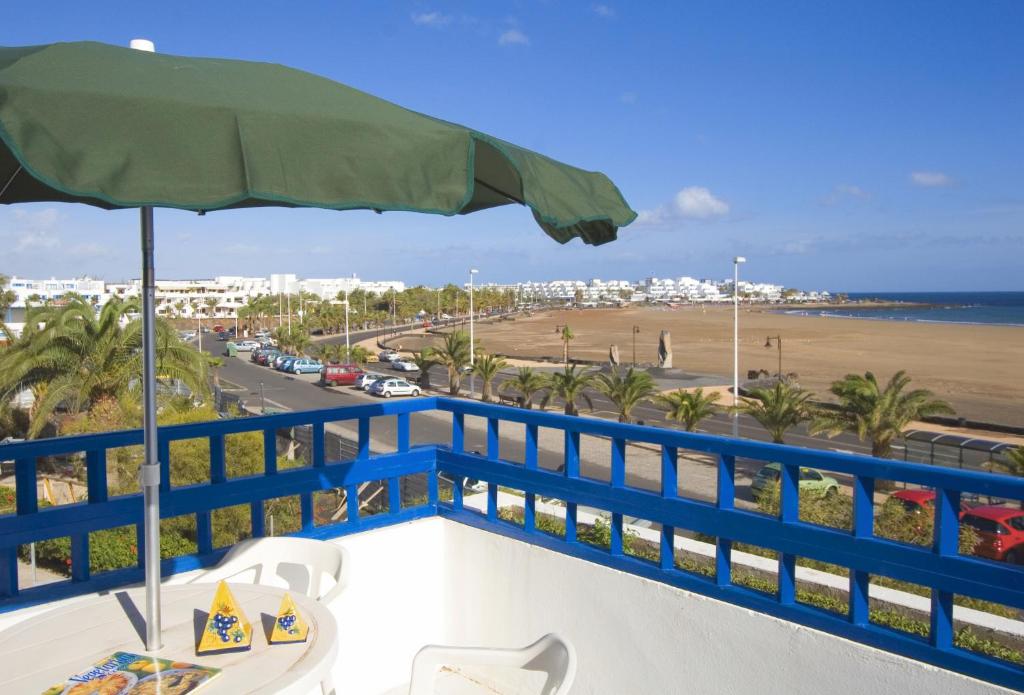 a balcony with a table and an umbrella and the beach at Apartamentos Club Pocillos in Puerto del Carmen