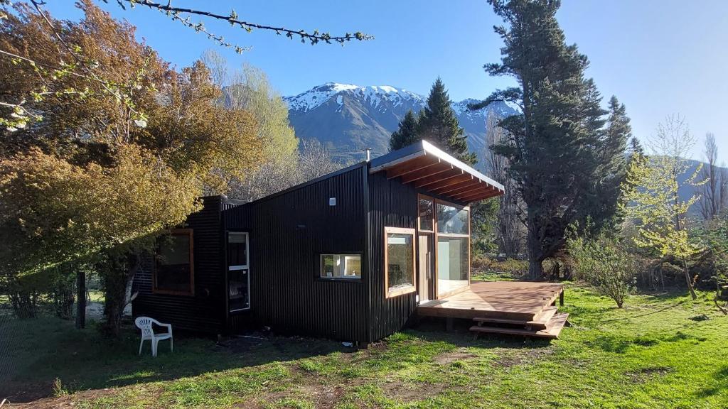 uma cabina preta com um deque e montanhas ao fundo em Alojamiento Chacra El Monje em El Hoyo