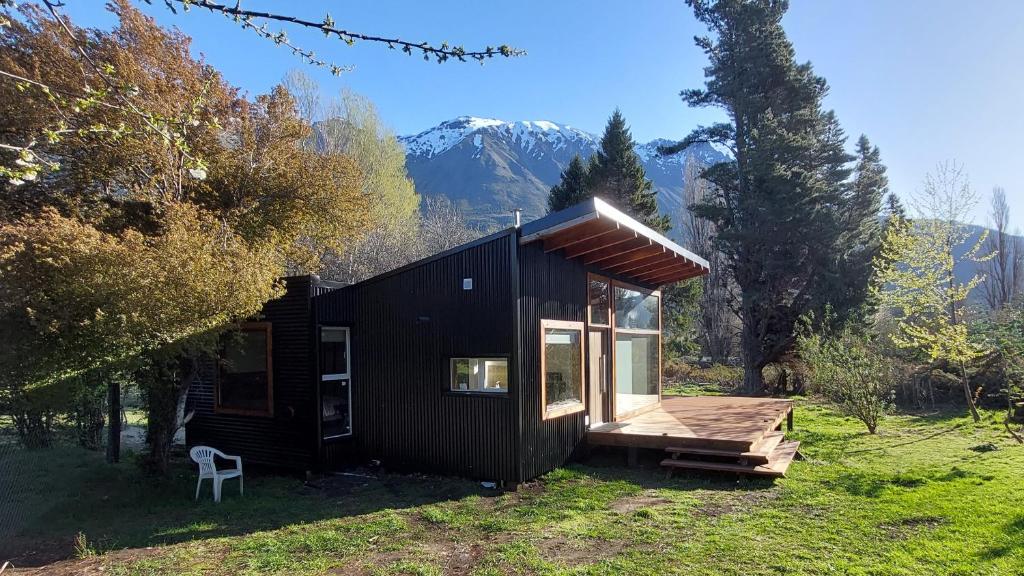 a black cabin with a deck and mountains in the background at Alojamiento Chacra El Monje in El Hoyo