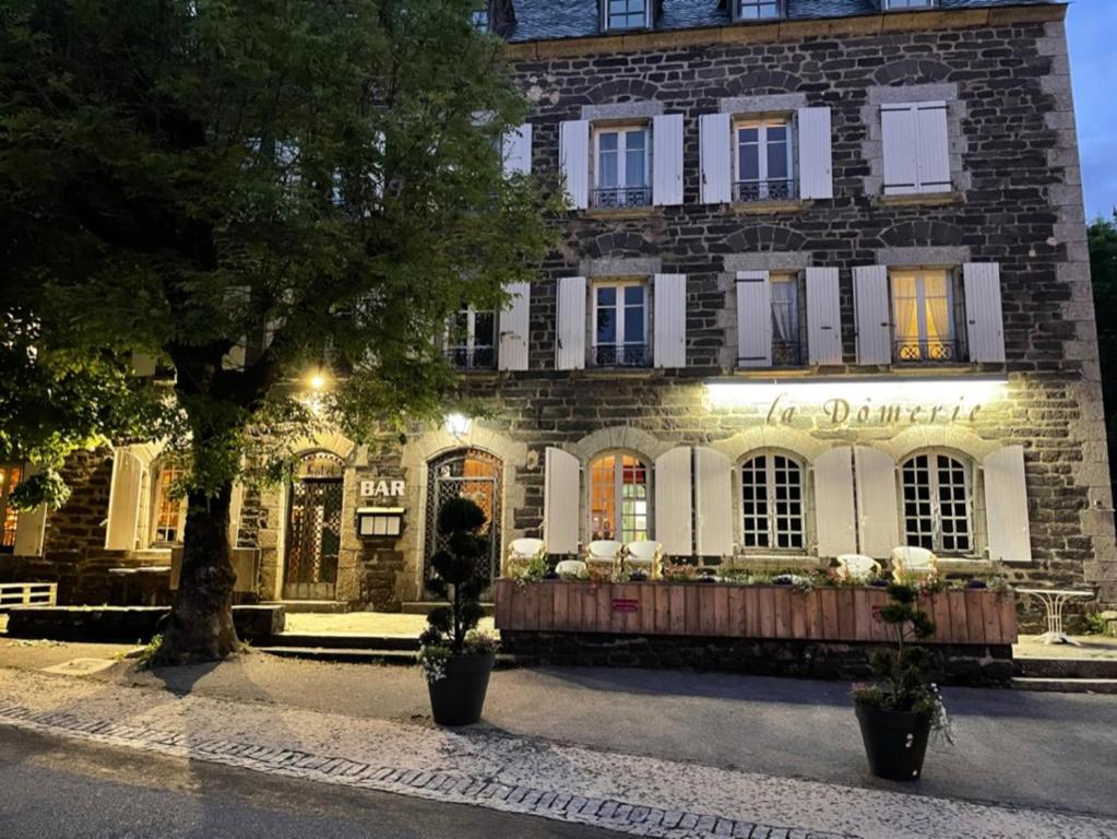 un gran edificio de ladrillo con un árbol delante de él en La Domerie - Maison d'hôtes en Aubrac