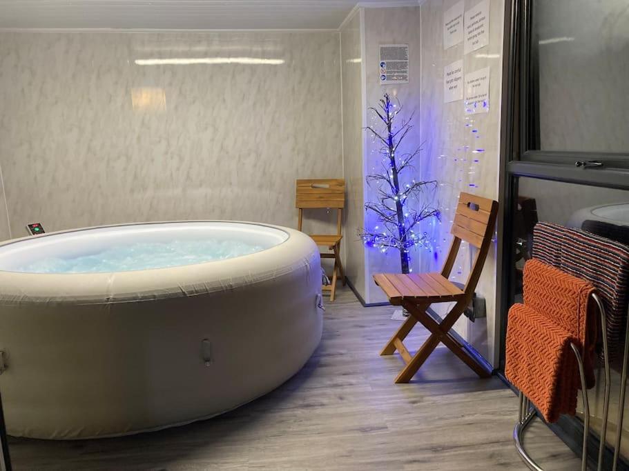 een groot bad in een kamer met een stoel bij 17 Cheerful 2 bed bungalow, hot tub/gym/pool table in Prestatyn