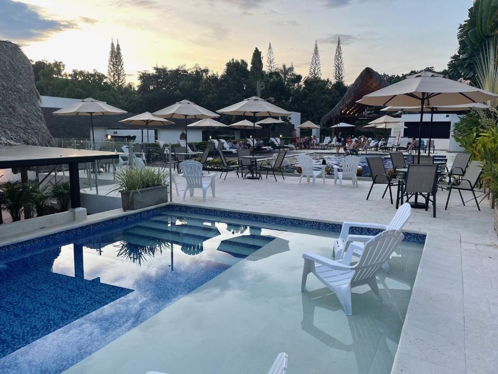 una piscina con sillas blancas, mesas y sombrillas en La Masia Hotel Boutique en Anapoima