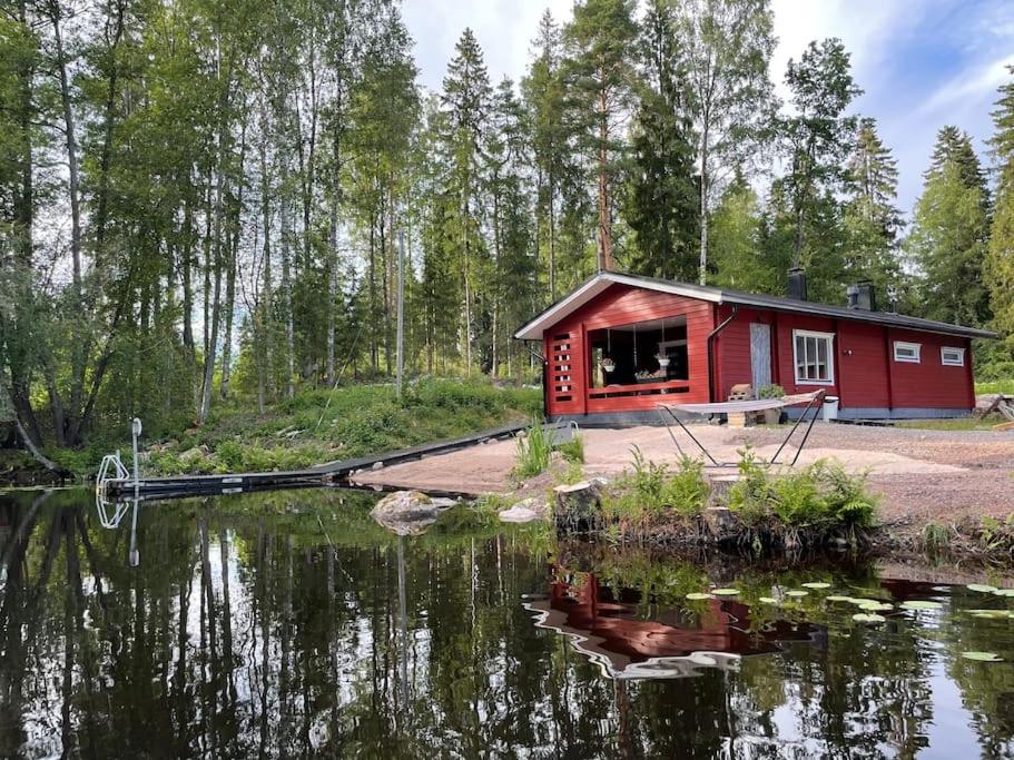 una cabina roja junto a un cuerpo de agua en Katiskosken joenrantamökki, en Hämeenlinna
