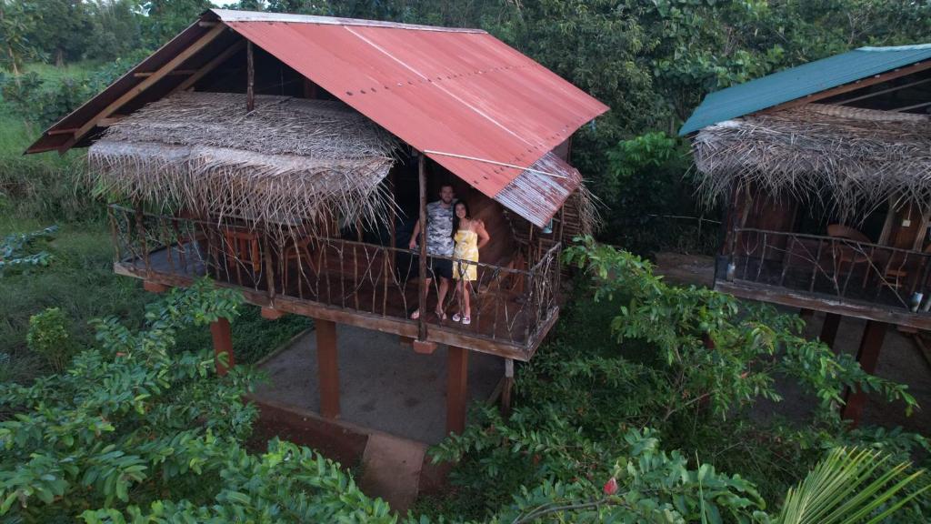 zwei Personen stehen auf einem Balkon eines Hauses mit rotem Dach in der Unterkunft Chena Huts Eco Resort in Sigiriya