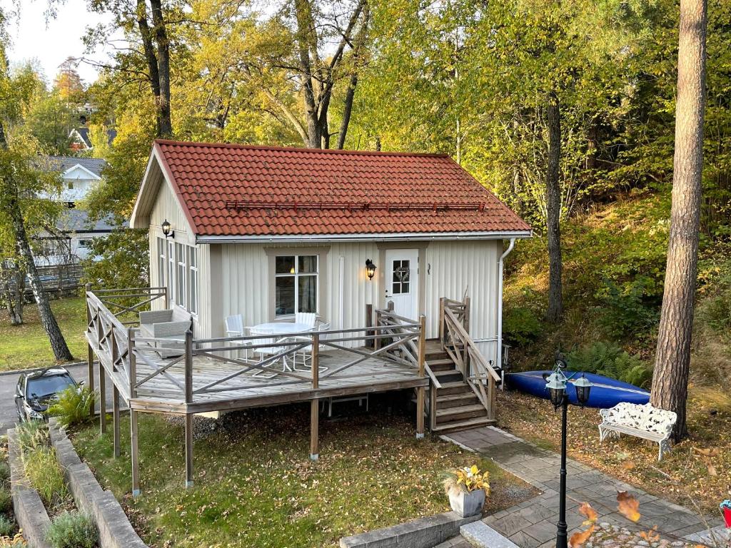 Cozy cabin, neighbour to lake & national park في Tyresö: منزل أبيض صغير مع سطح و قارب
