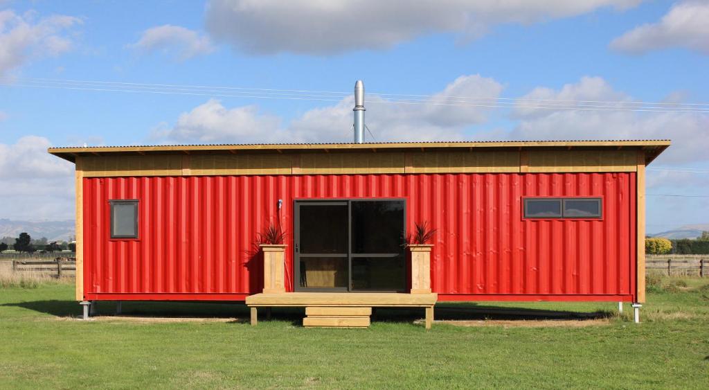 un cobertizo rojo con una ventana en un campo en Luxury Container Cabin, en Masterton