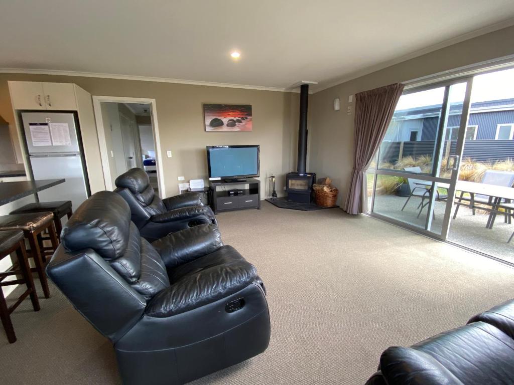 a living room with a black leather couch and a television at Rocking it On Rhoboro in Twizel