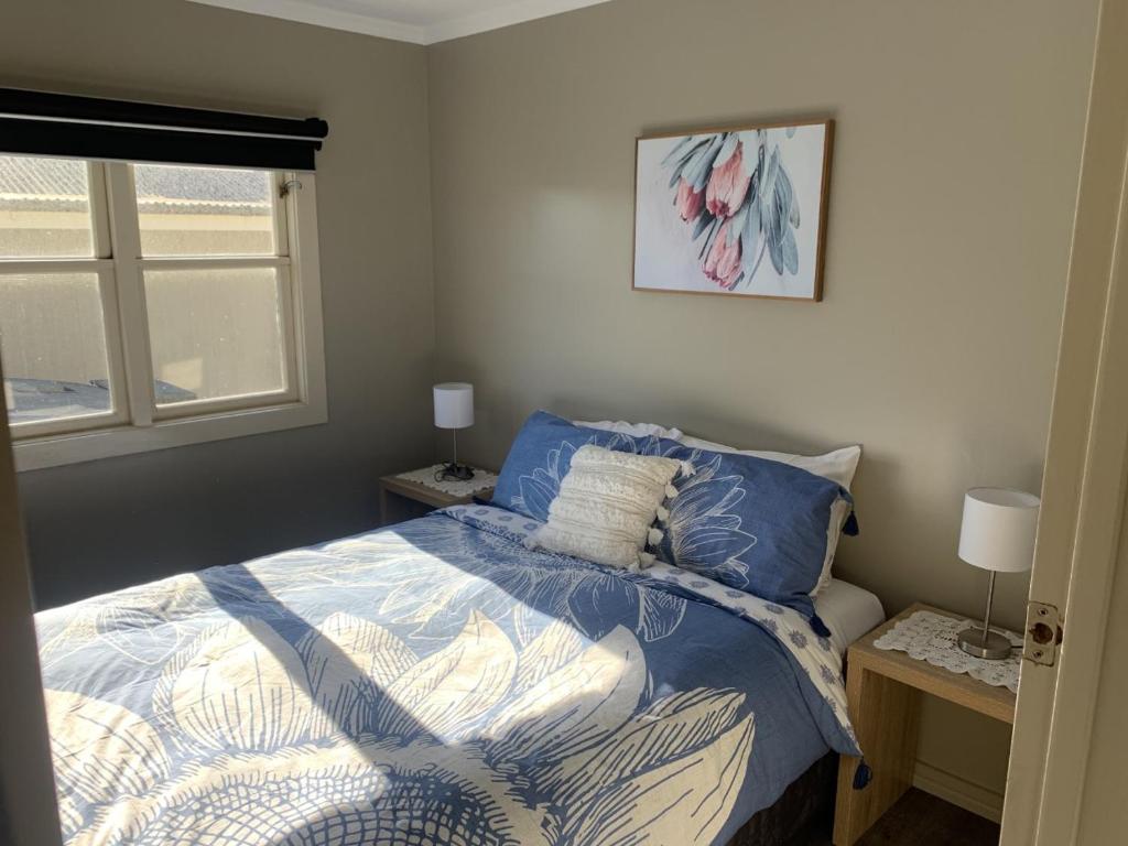 a bedroom with a bed with a blue comforter and a window at Wedderburn Farm Stay in Wedderburn