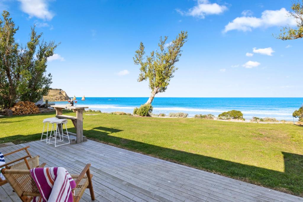 un patio con mesa y sillas y la playa en Karitane Cottage - Karitane Holiday Home en Karitane