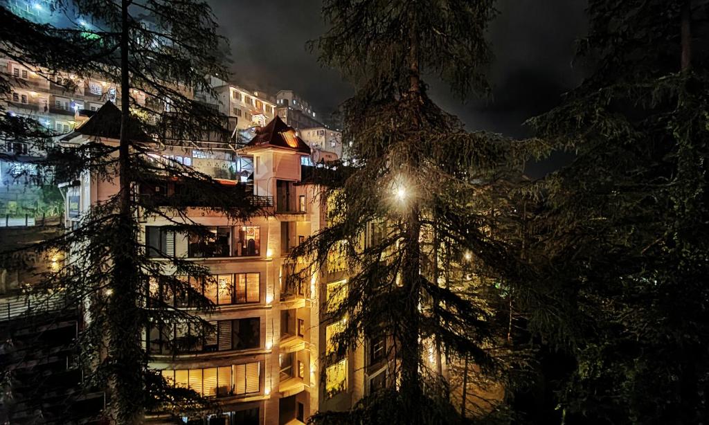 Hotel Royale Retreat - Luxury Hotel In Shimla في شيملا: مبنى طويل في الليل به شجرة