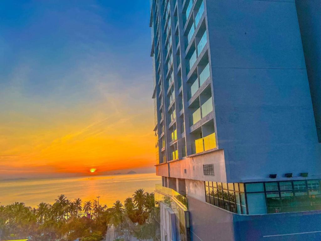 un edificio alto con una puesta de sol en el fondo en Alana Nha Trang Beach Hotel, en Nha Trang