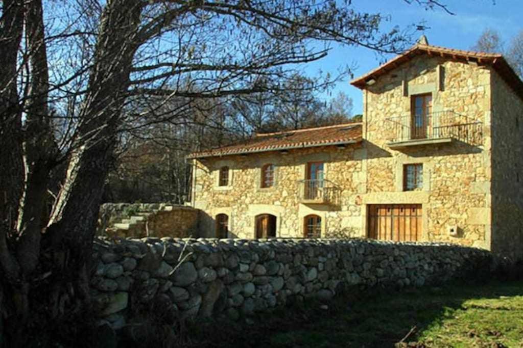 a stone house with a stone wall and a tree at La Torre del Molino es una casa rural ubicada sobre un antiguo molino in Tormellas