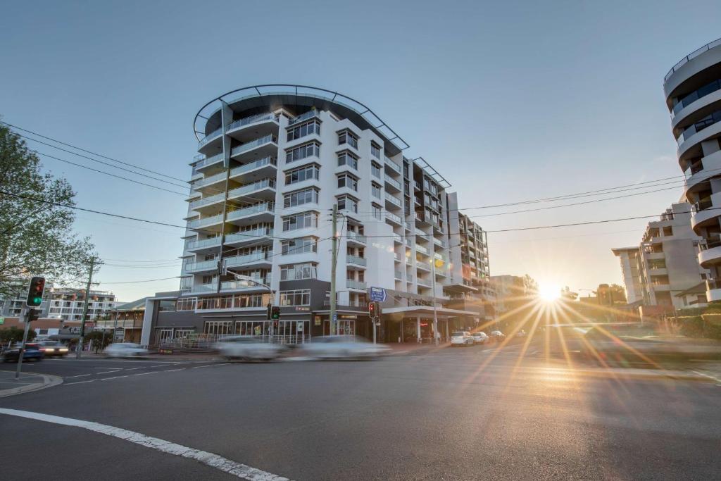 a city street with a tall building with the sun setting at Adina Apartment Hotel Wollongong in Wollongong