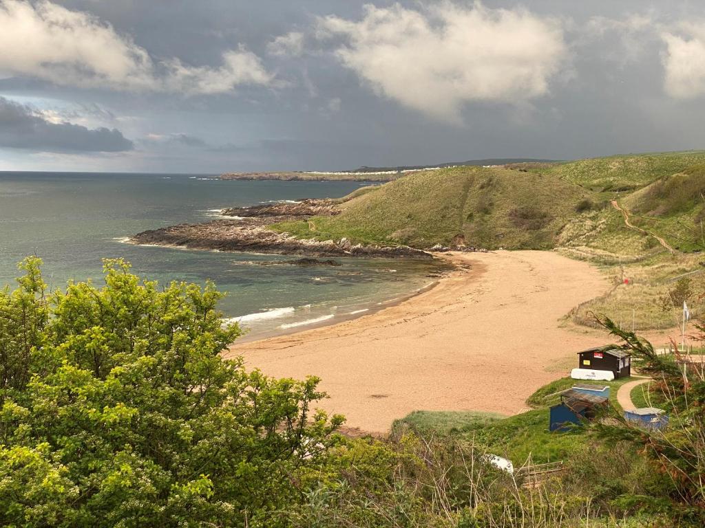 a beach with a house on a hill next to the ocean at 1 The Bay - Stunning contemporary flat on the Scottish coast in Coldingham