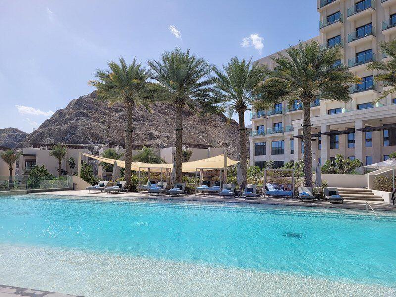 une piscine bordée de palmiers et un hôtel dans l'établissement Address Beach Resort Residence Fujairah, à Fujaïrah