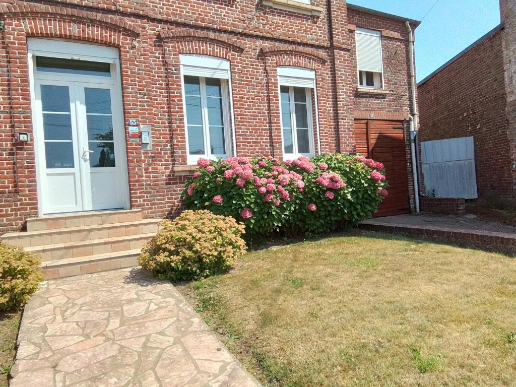 a brick house with a white door and pink flowers at Charmant studio centre bourg in Woincourt
