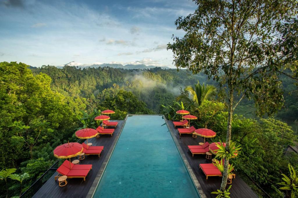 a swimming pool with red chairs and umbrellas at Buahan, a Banyan Tree Escape in Payangan