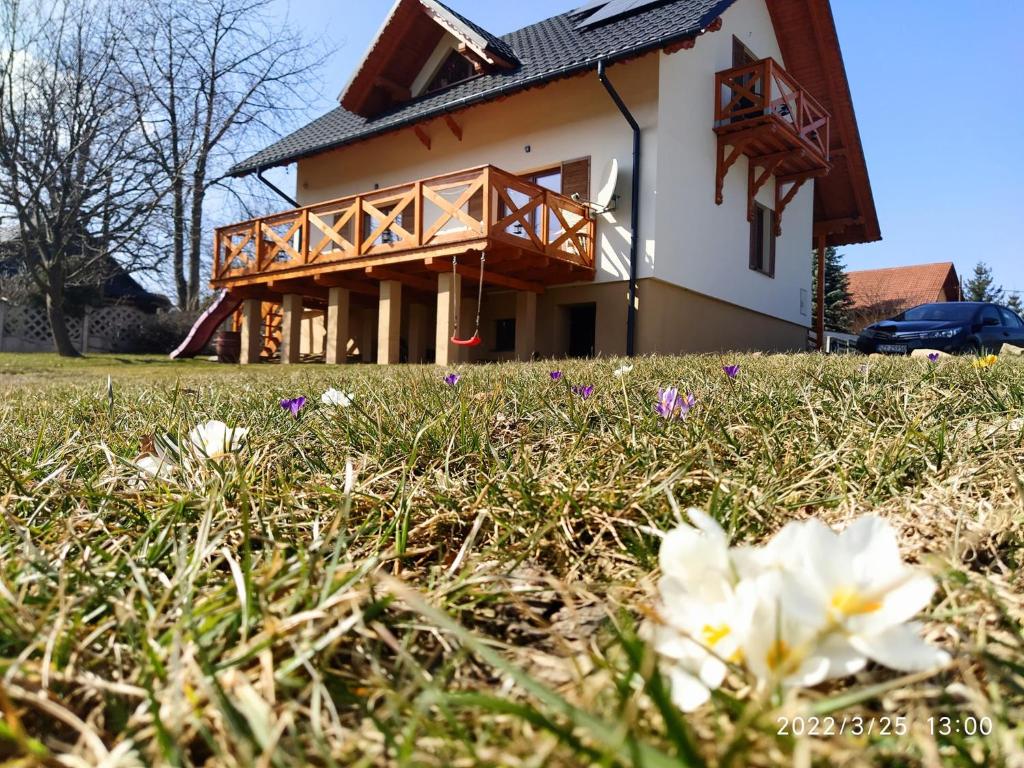 ein Haus mit einem Balkon und Blumen im Gras in der Unterkunft Leśny Domek 