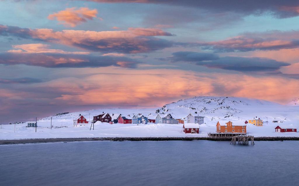 a small town in the snow with a cloudy sky at Kongsfjord Arctic Lodge in Kongsfjord